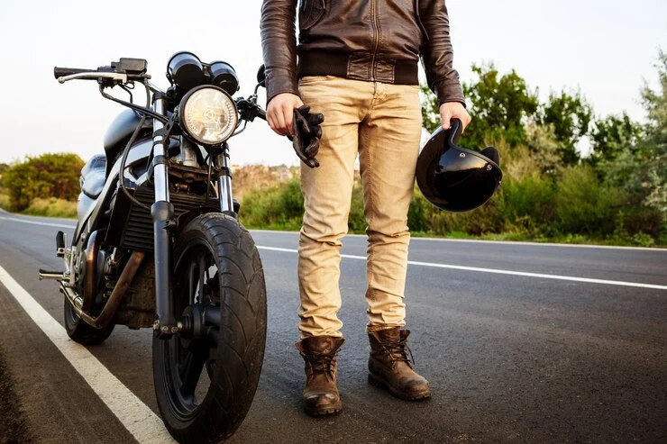 mann poserer i nærheten av motorsykkelen sin på landsvei.